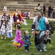 Image of adult Powwow dancer in full regalia dancing with two young girls